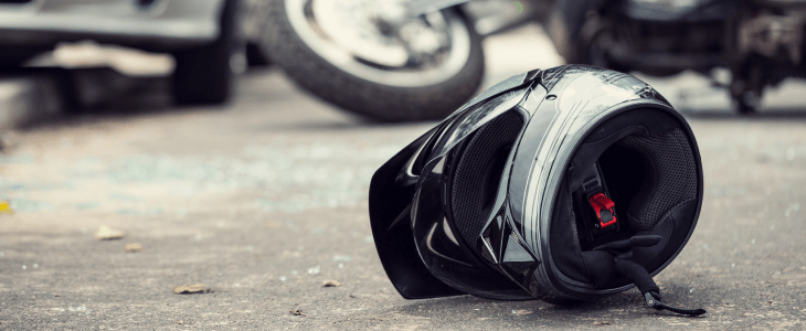 Motorcycle helmet on the road in front of a fallen motorcycle and car.