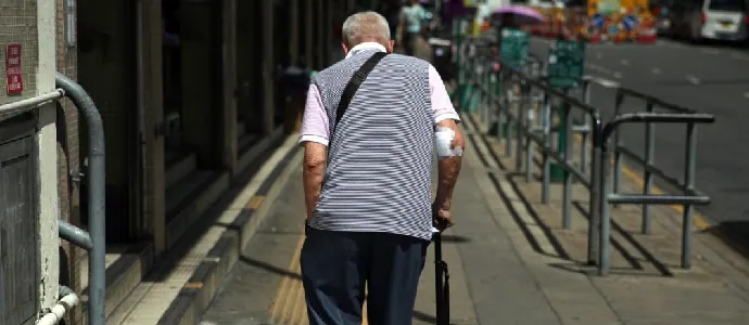 Older adult walking with a cane along a city sidewalk